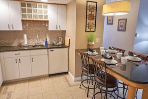 A kitchen with white cabinets, a tiled backsplash, and a dining area with a table set for four. - Deluxe Suite standard room (Fairhaven)