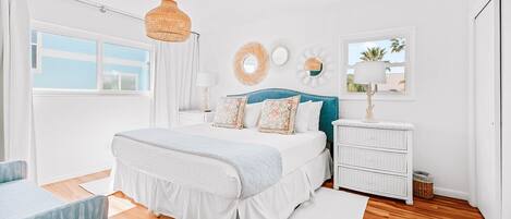 Un dormitorio con cama, mesitas de noche, cómoda, lámpara colgante y ventana con vistas.