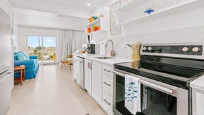 A modern kitchen with white cabinetry, a black stove, and a dining area with a blue sofa and a small table.
