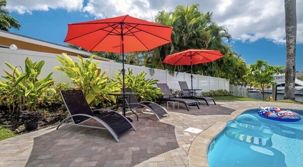 A poolside area with lounge chairs, red umbrellas, and a pool with a floating ring. - Luxury Waterfront With Heated Pool Fort Lauderdale FL (Fort Lauderdale)