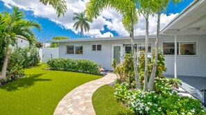 A modern house with a well-maintained lawn, a curved pathway, and a variety of plants and trees.