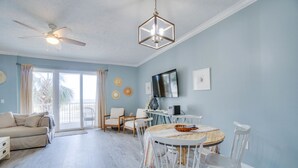 A spacious living room with a ceiling fan, a dining table with white chairs, and a large window with curtains. - Gorgeous condo with gulf views, pool & hot tub in Mexico Beach. Sleeps 6. (Mexico Beach)