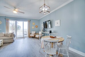 A spacious living room with a ceiling fan, a dining table with white chairs, and a large window with curtains. - Gorgeous condo with gulf views, pool & hot tub in Mexico Beach. Sleeps 6. (Mexico Beach)