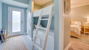 A bedroom with a bunk bed, a door with a frosted glass panel, and a small bedside table with a lamp. - Gorgeous condo with gulf views, pool & hot tub in Mexico Beach. Sleeps 6. (Mexico Beach)