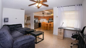 Sala de estar com sofá, mesinha, ventilador de teto e vista para a cozinha.