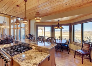 A spacious kitchen with a granite countertop, wooden ceiling, and large windows offering a view of the outdoors.