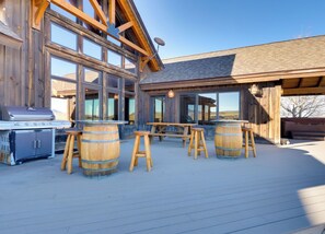 A wooden deck with a barbecue grill, wooden barrels, and a large window overlooking a landscape.