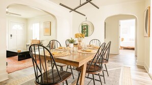 Un coin repas avec une table en bois, des chaises noires, un luminaire suspendu et un miroir au mur.