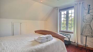 Un dormitorio con cama, ventana con cortinas, una silla de metal y un maniquí.