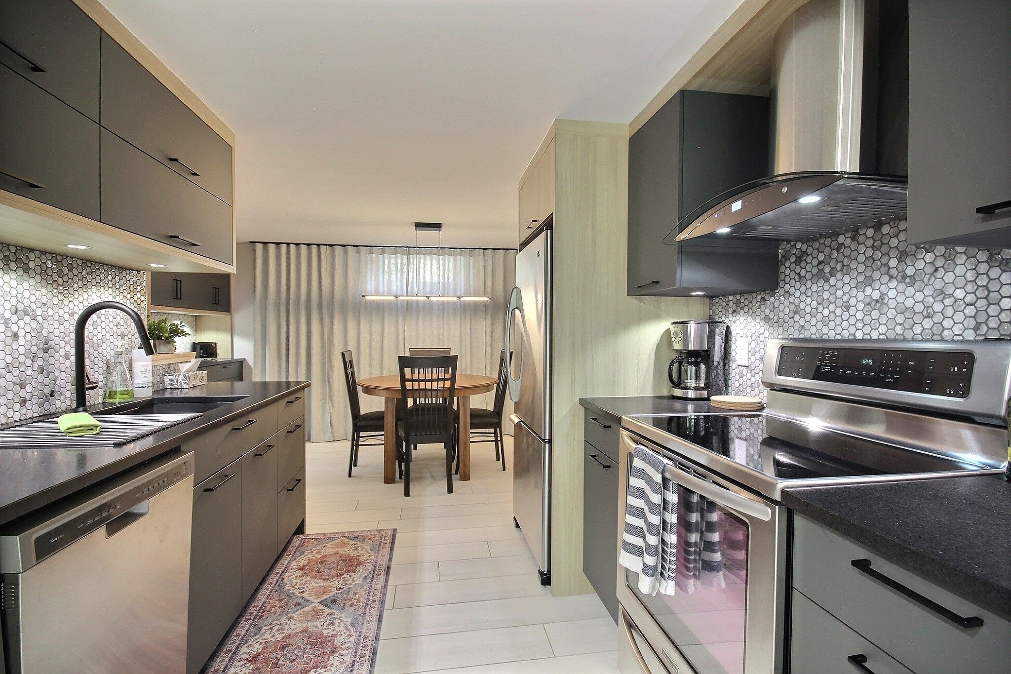 A modern kitchen with a dining area, stainless steel appliances, and a hexagonal tile backsplash.