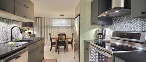 Una cocina moderna con comedor, electrodomésticos de acero inoxidable y un salpicadero de azulejos hexagonales.