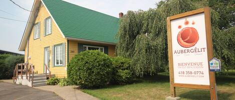 A yellow building with a green roof, a signboard with contact information, and a well-maintained lawn.
