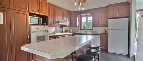 A kitchen with wooden cabinets, a large island with stools, a microwave, a stove, and a refrigerator.