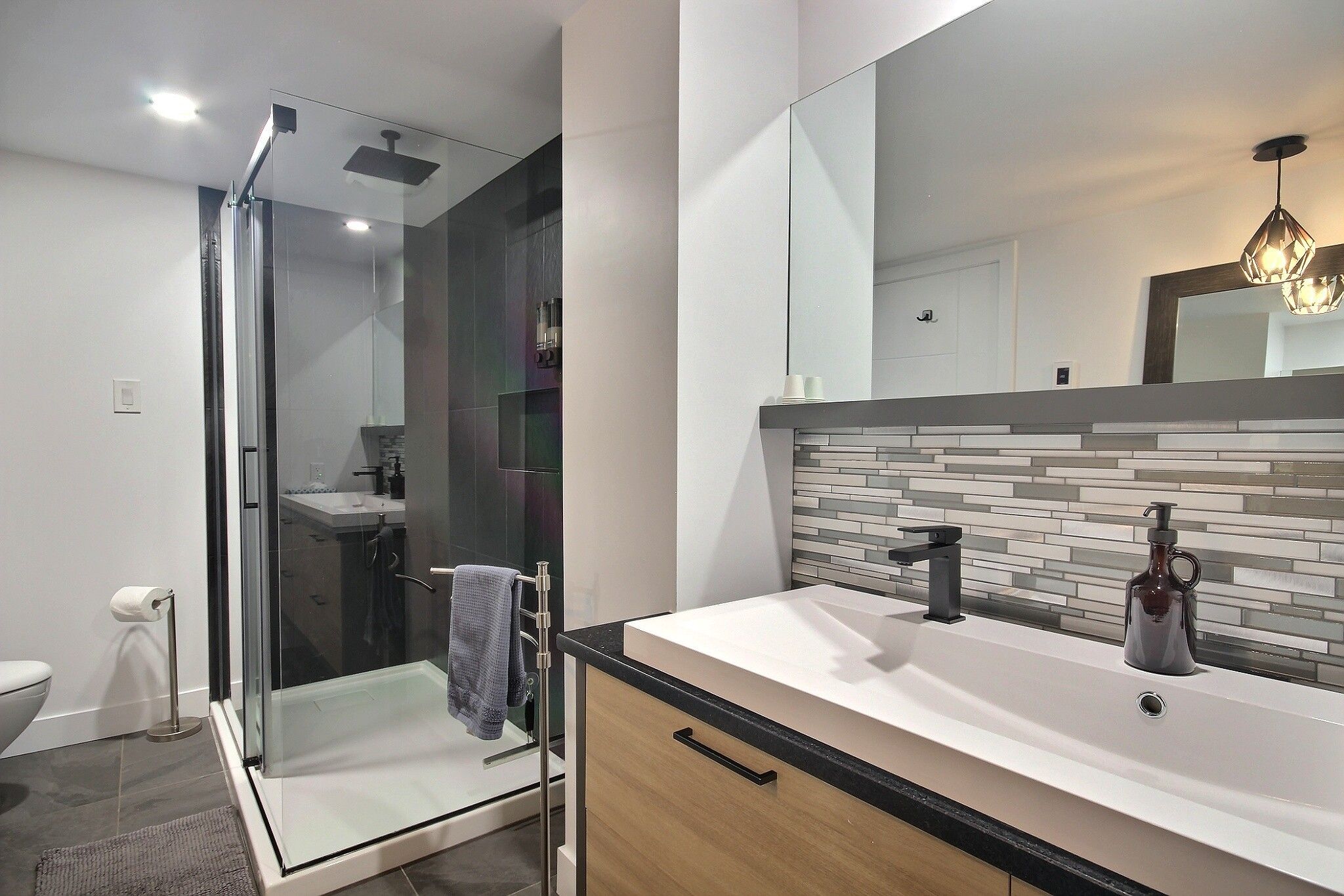 A modern bathroom with a glass shower enclosure, a vanity with a tiled backsplash, and a large mirror.