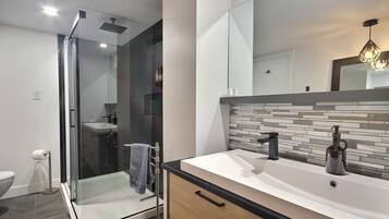 A modern bathroom with a glass shower enclosure, a vanity with a tiled backsplash, and a large mirror.