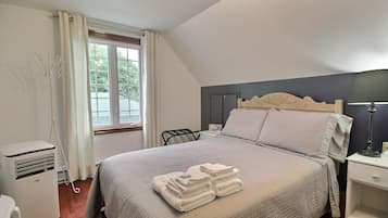 Una cama bien hecha con cabecera, una mesita de noche con lámpara y una ventana con cortinas.