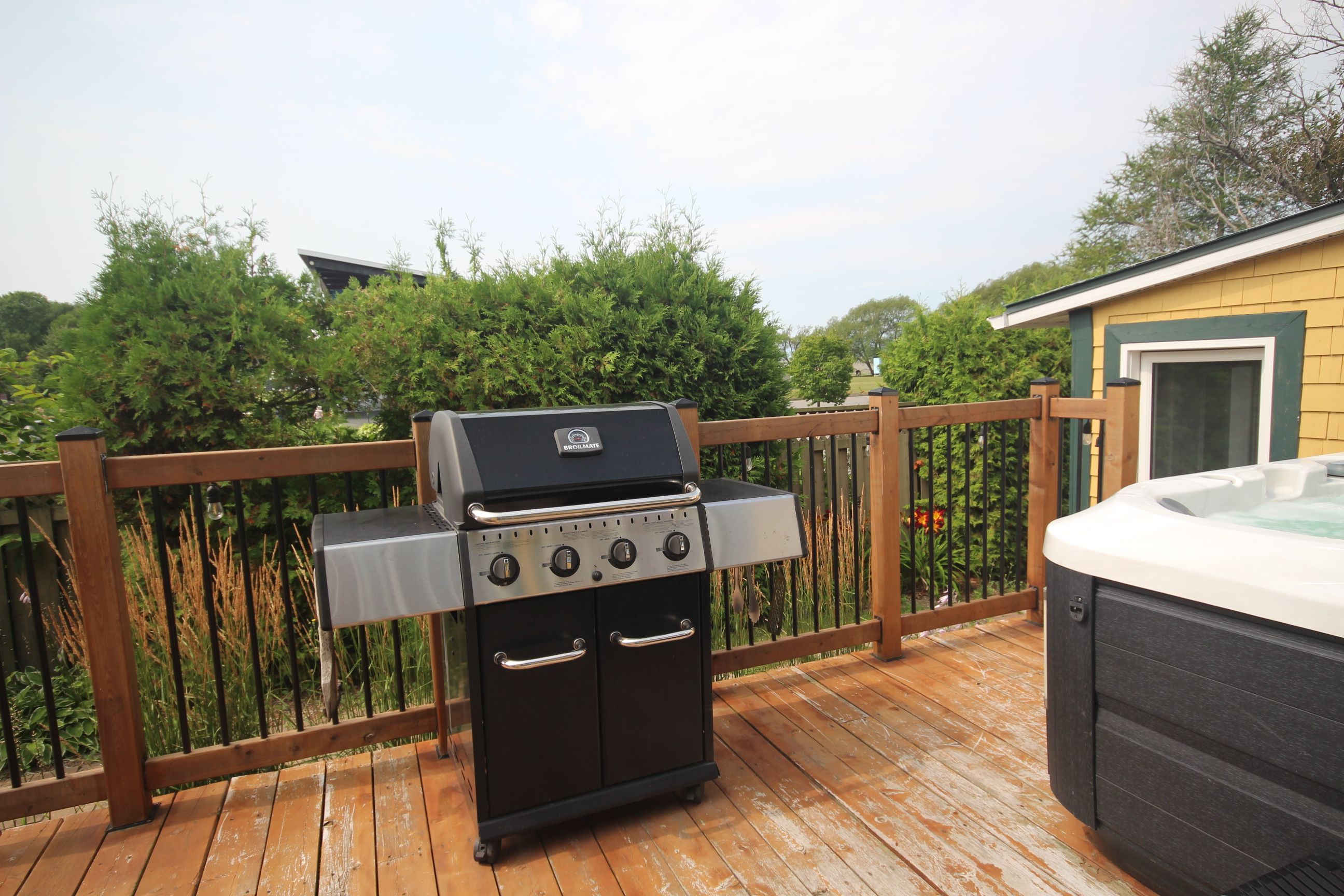 A barbecue grill with four burners and a hot tub on a wooden deck.