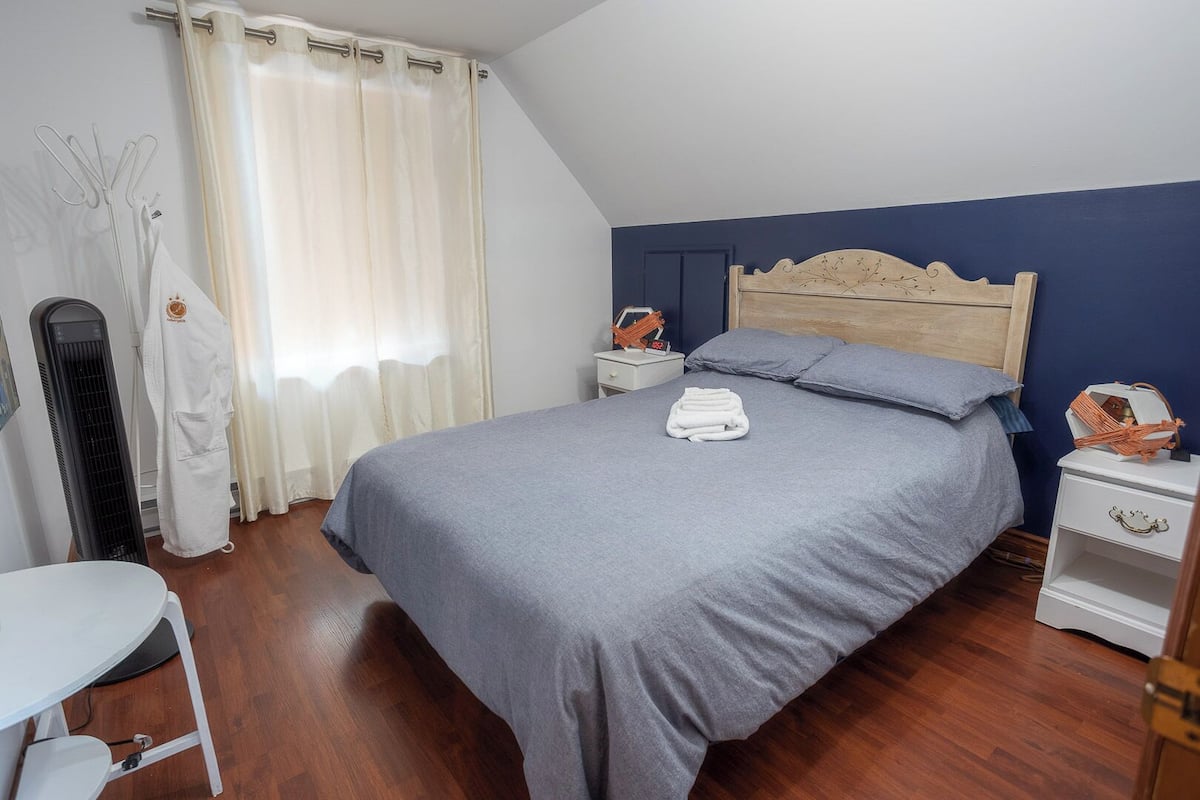 A bedroom with a bed, a nightstand, a chair, a heater, and a window with curtains.