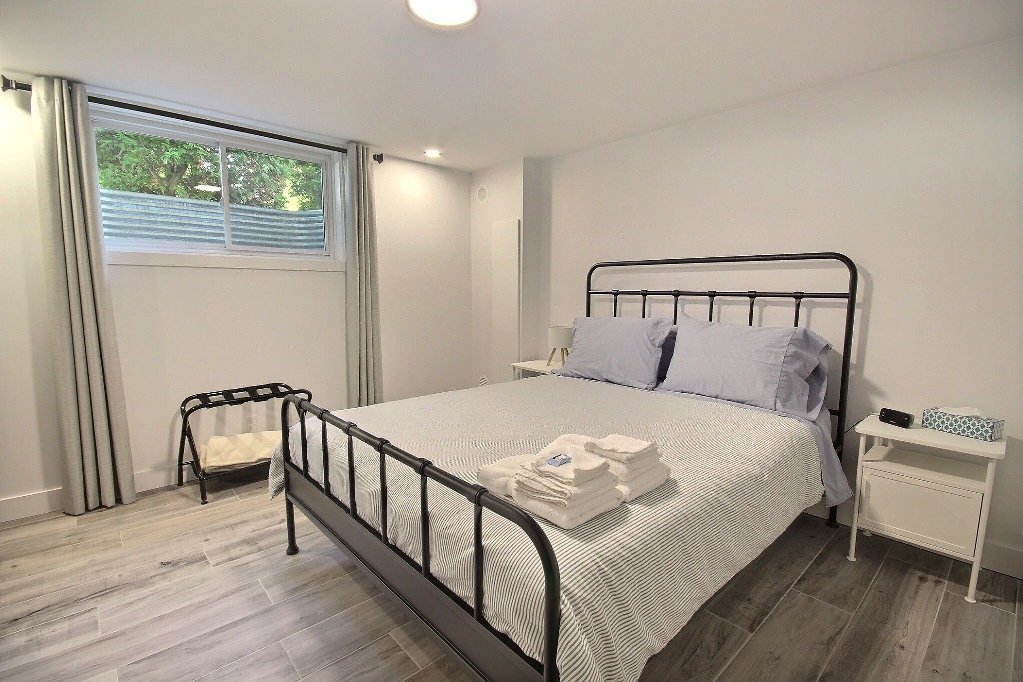 A modern bedroom with a metal bed frame, a bedside table, and a window with curtains.