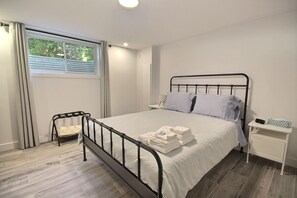 A modern bedroom with a metal bed frame, a bedside table, and a window with curtains. - Aubergélit (Saint Jean Port Joli)