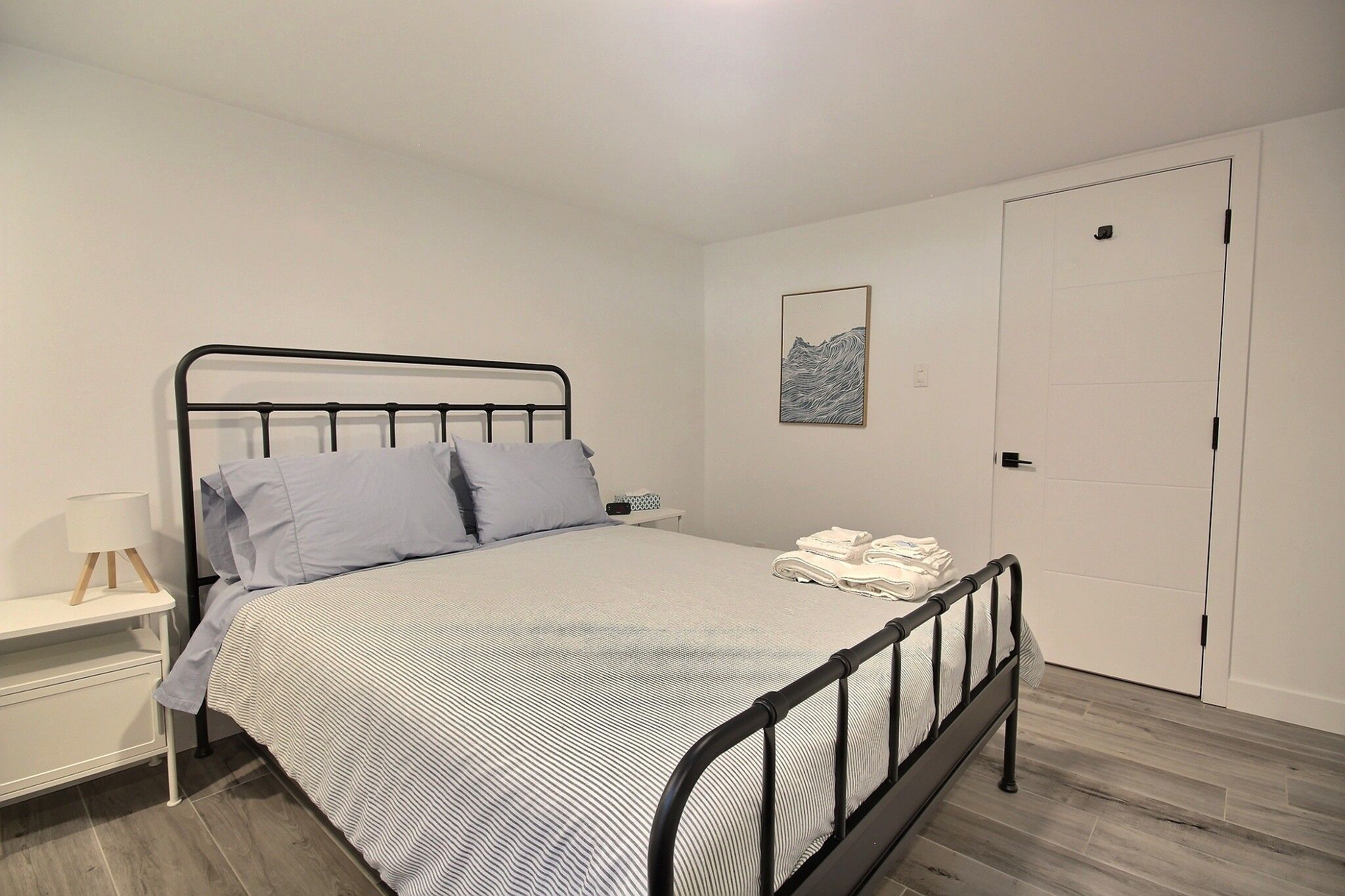 A single bed with a metal frame, a bedside table with a lamp, and a door in the background.