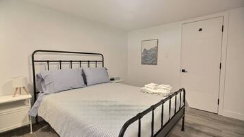 A single bed with a metal frame, a bedside table with a lamp, and a door in the background.