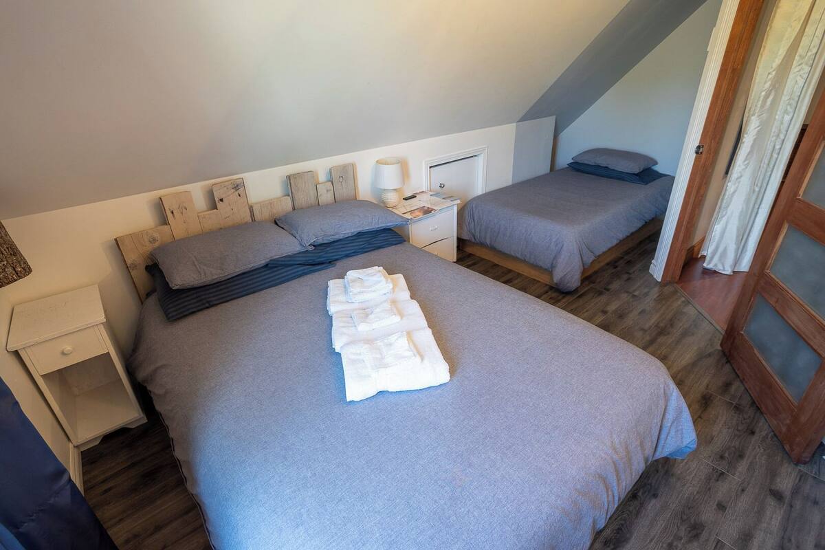 A bedroom with a large bed, a smaller bed, a nightstand, and a wooden headboard.