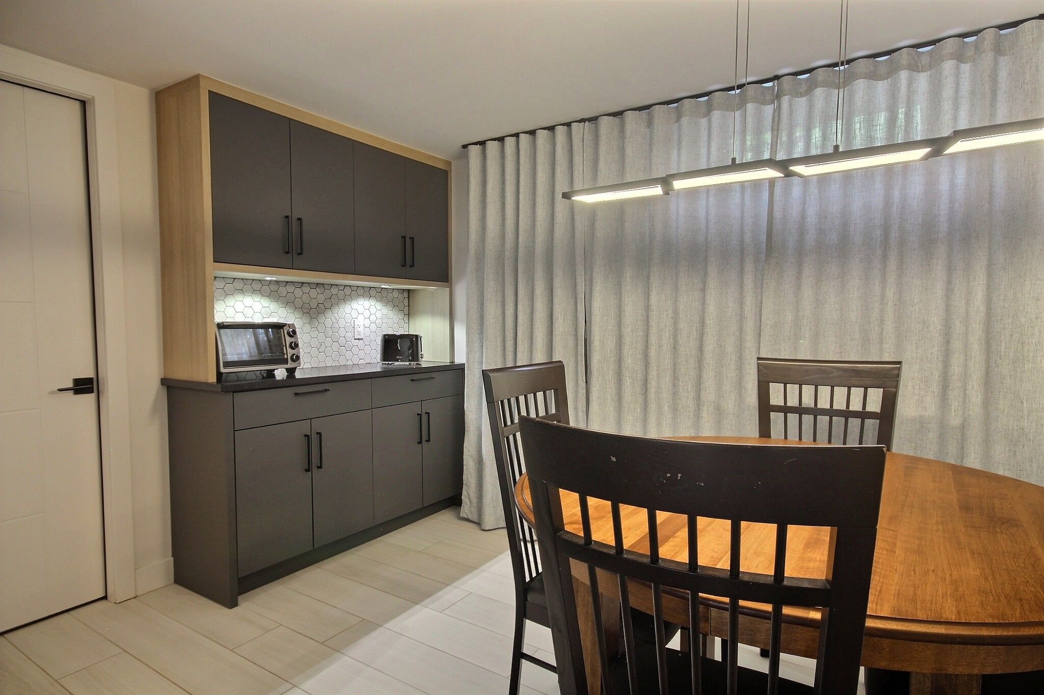 Una cocina compacta con electrodomésticos modernos, una mesa de comedor con sillas y un amplio ventanal con cortinas.