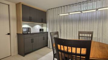 Una cocina compacta con electrodomésticos modernos, una mesa de comedor con sillas y un amplio ventanal con cortinas.