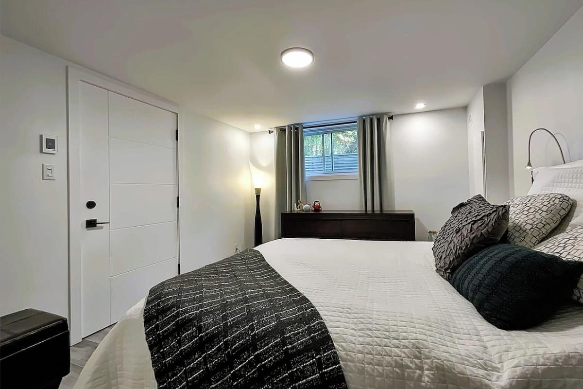 A bedroom with a bed, bedside table, lamp, window with curtains, and a door with a lock.