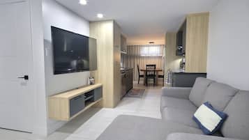A modern living room with a flat-screen TV, grey sofa, and a dining area with a table and chairs.