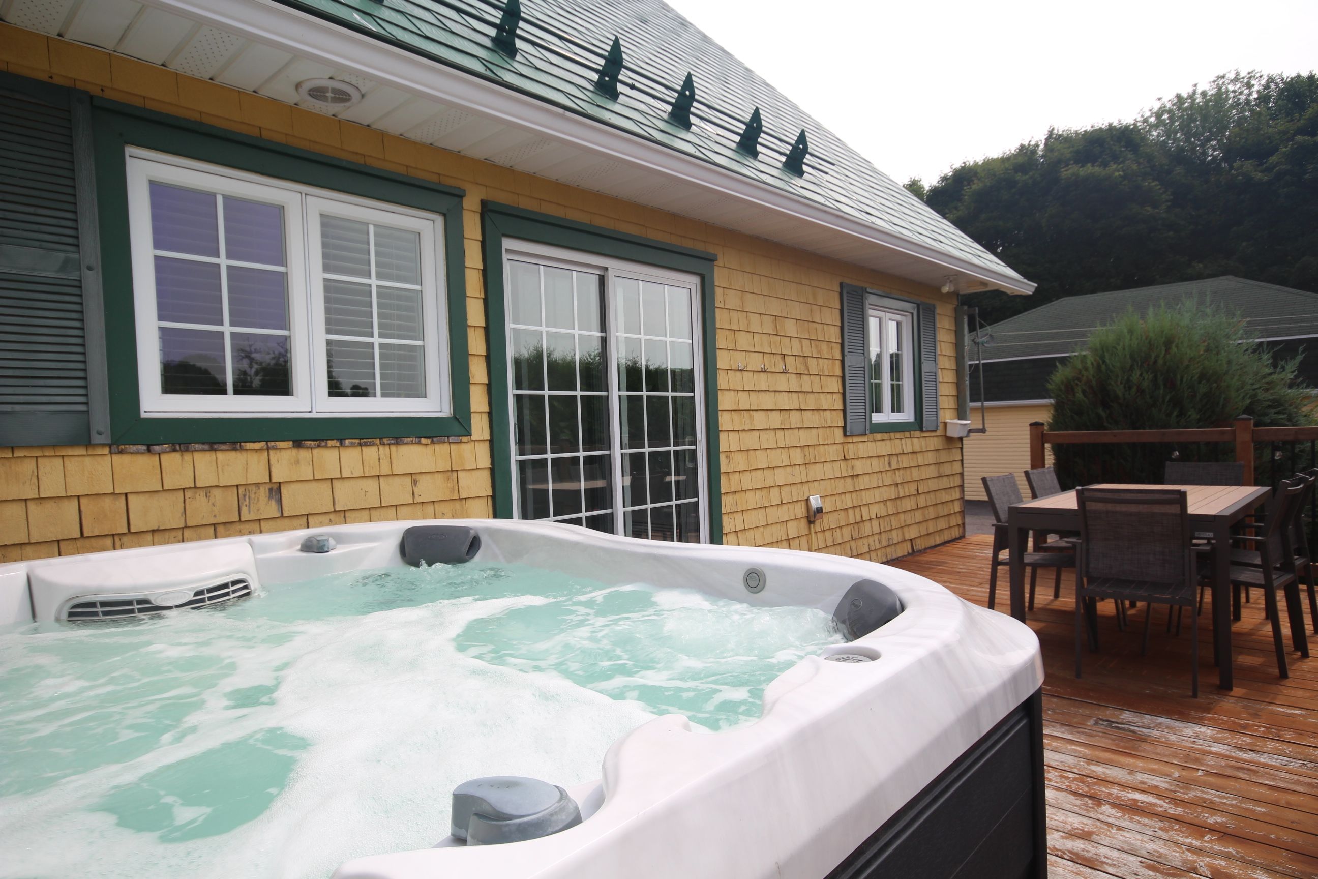 Un jacuzzi en una terraza de madera con una casa al fondo.