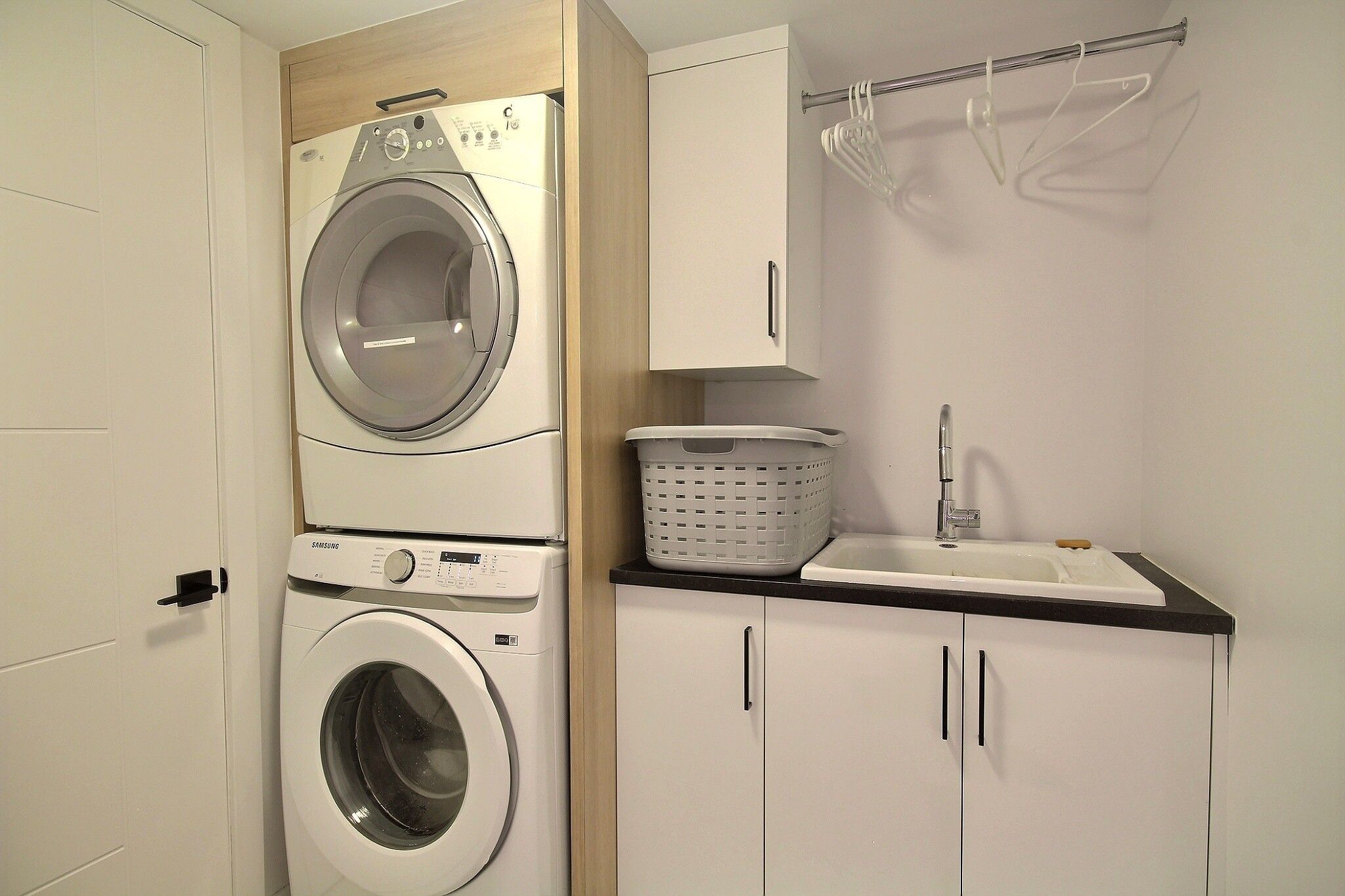 A laundry room with a front-loading washing machine, a dryer, a sink, and a cabinet.