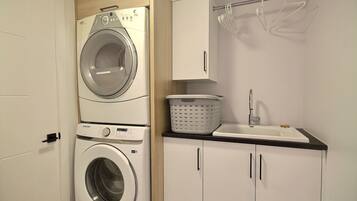 A laundry room with a front-loading washing machine, a dryer, a sink, and a cabinet.