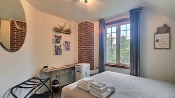 A bedroom with a bed, a desk, a chair, a heater, a window with curtains, and artwork on the walls.