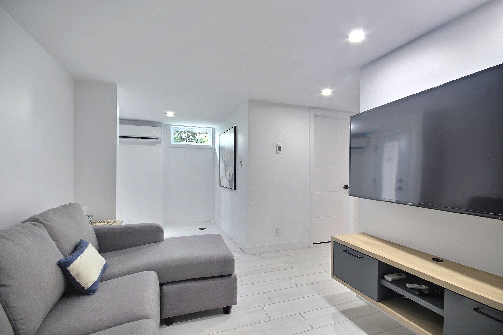 A modern living room with a grey sofa, a flat-screen TV, and a minimalist design.