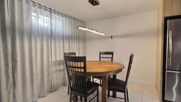 Een eetgedeelte met een ronde houten tafel, vier stoelen, een moderne hanglamp en een roestvrijstalen koelkast.