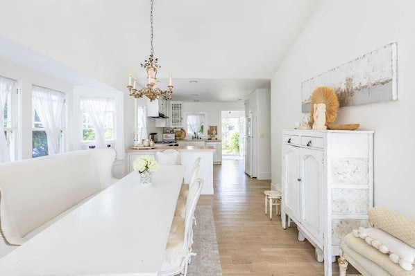 Une cuisine spacieuse et bien éclairée, avec des meubles blancs, un îlot central et un lustre.