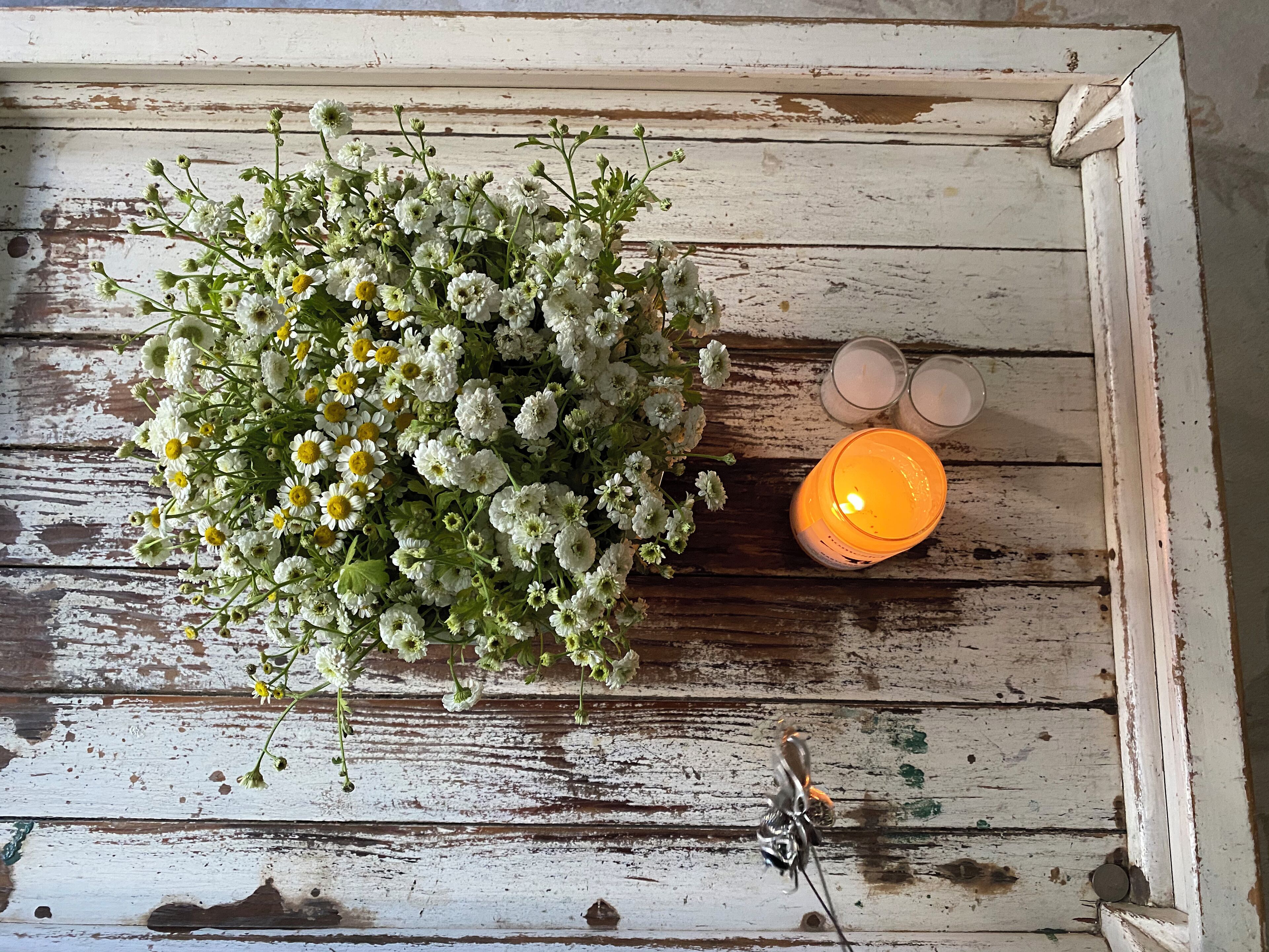 Una superficie de madera rústica con un arreglo floral y dos velas encendidas.