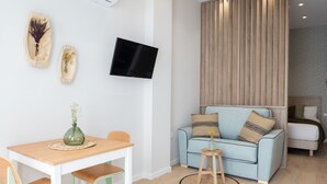 A modern living room with a light blue sofa, a wooden dining table with two chairs, a mounted flat-screen TV, and a decorative wall piece. - The Sea Rooms VIII | AC & WIFI | 15 min Beach (Valencia)