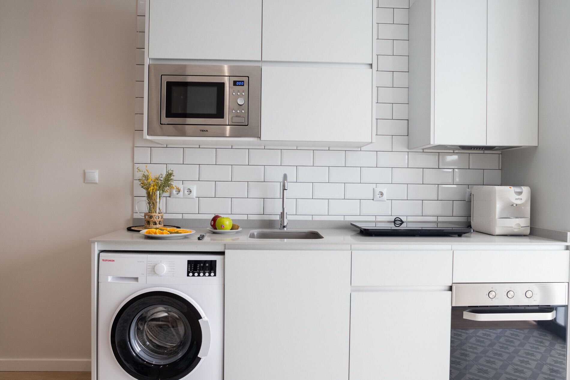 Een functionele keuken met een wasmachine, een magnetron en een vaatwasser.