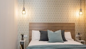 Une chambre à coucher comprenant un lit, deux tables de chevet, une commode, un climatiseur fixé au mur et un papier peint à motifs.