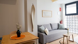 Un salon moderne avec un canapé gris, une table en bois sur laquelle est posé un vase, et une œuvre d’art abstraite encadrée accrochée au mur.