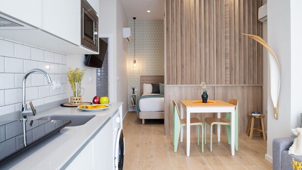 Une cuisine compacte dotée d’appareils électroménagers modernes, un coin repas avec une table et des chaises en bois, et un espace nuit confortable avec un lit et une table de chevet.