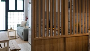 Una sala de estar moderna con un separador de madera, un sofá, una mesa de centro y un comedor con un banco y una mesa.