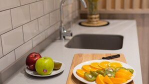 Una cocina con baldosas blancas, una tabla de madera con fruta y un lavamanos.