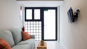 A modern interior with a grey sofa, a wooden side table, and a black door with a grid pattern.