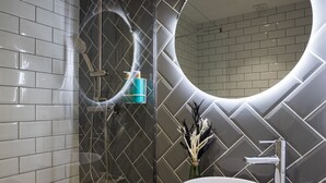 A modern bathroom with a large mirror, a white sink, and a shower with a handheld showerhead.