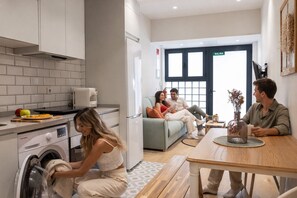 A modern kitchen with a washing machine, a dining area with a table and chairs, and a living room with a sofa and a coffee table.