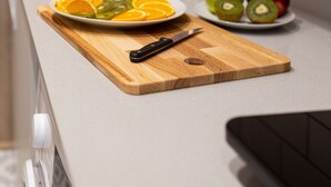 A kitchen counter with a cutting board, a knife, and plates of sliced fruits.
